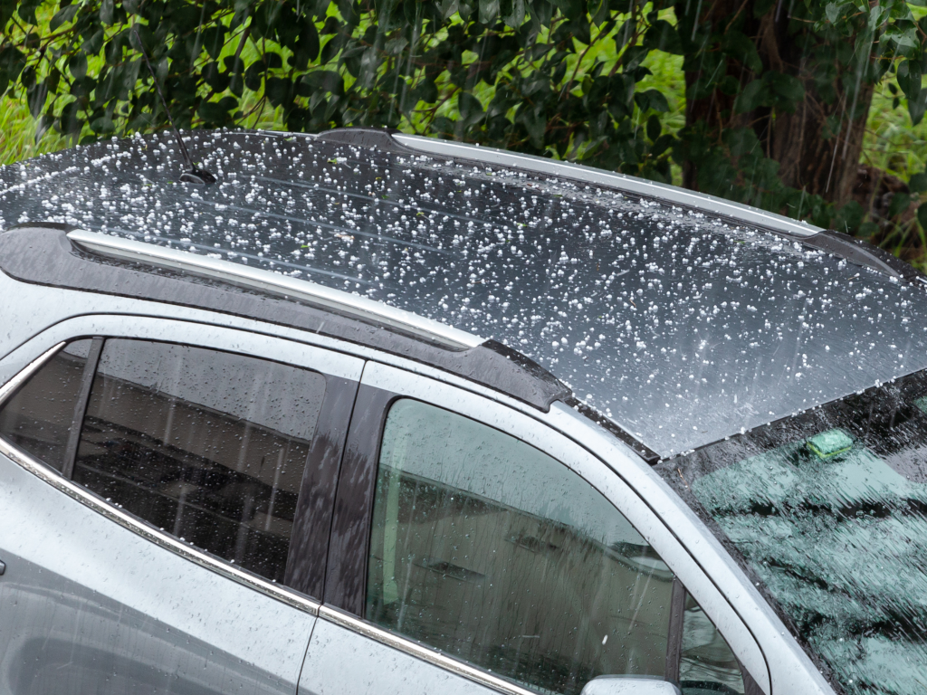 Car roof covered with hailstones during a hailstorm, showing visible hail damage on the vehicle&rsquo;s surface.